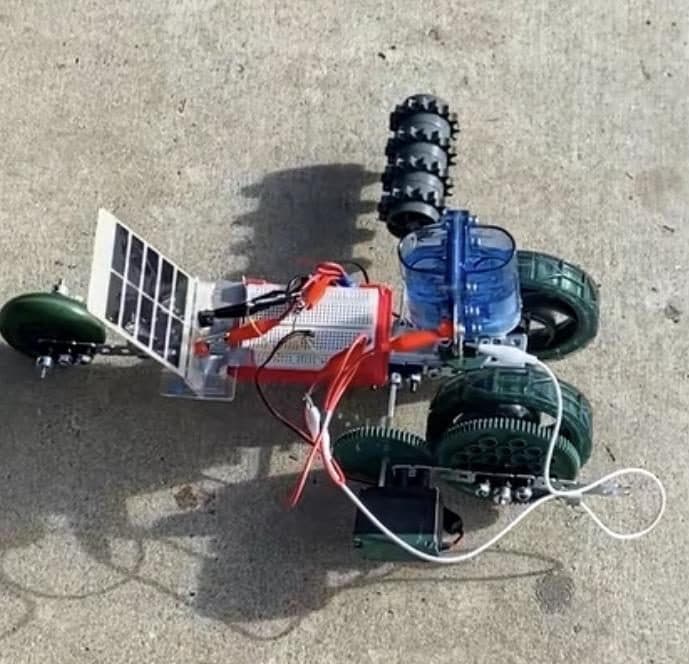 Close-up of a small solar-and-hydro racecar chassis with a solar panel, breadboard, and green wheels.